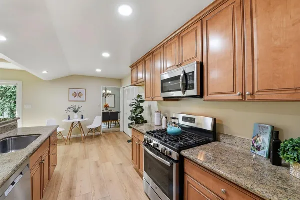 a kitchen with stainless steel appliances granite countertop a stove top oven a sink a dining table and chairs with wooden floor