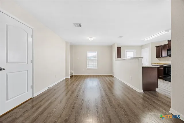 a view of empty room with wooden floor and kitchen