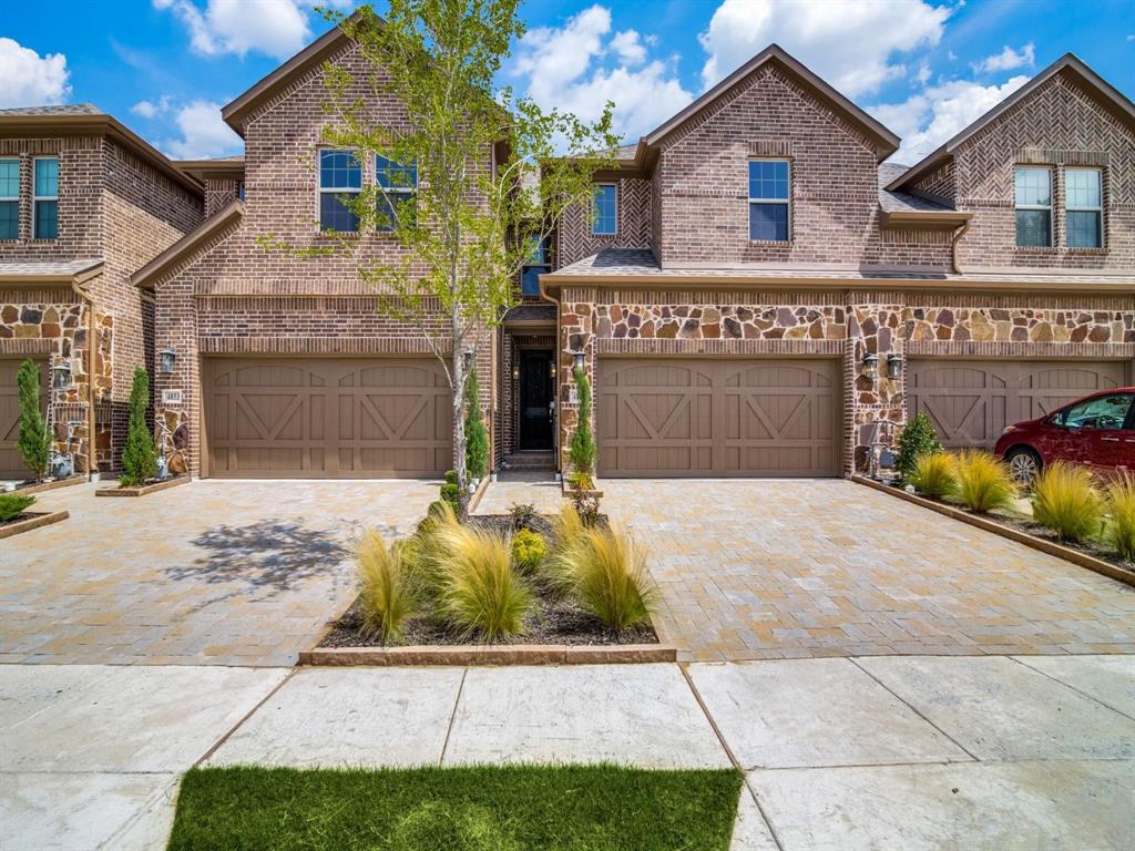 View of front of house featuring an attached garage, brick siding, and decorative driveway
