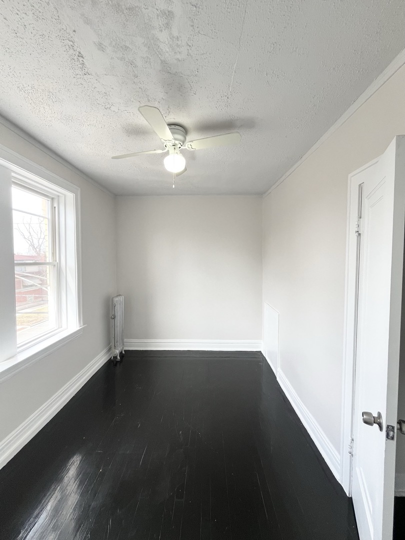 4134 West 24th Place, Unit E2 Chicago, IL 60623 - Photo 4 of 9 an empty room with wooden floor fan and windows