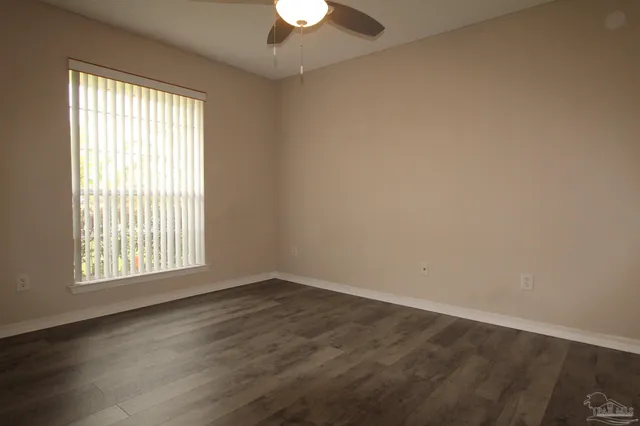 an empty room with wooden floor chandelier fan and windows