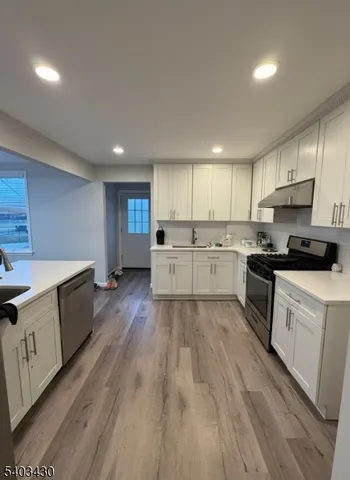 a kitchen with granite countertop a stove top oven a sink dishwasher and a refrigerator with wooden floor