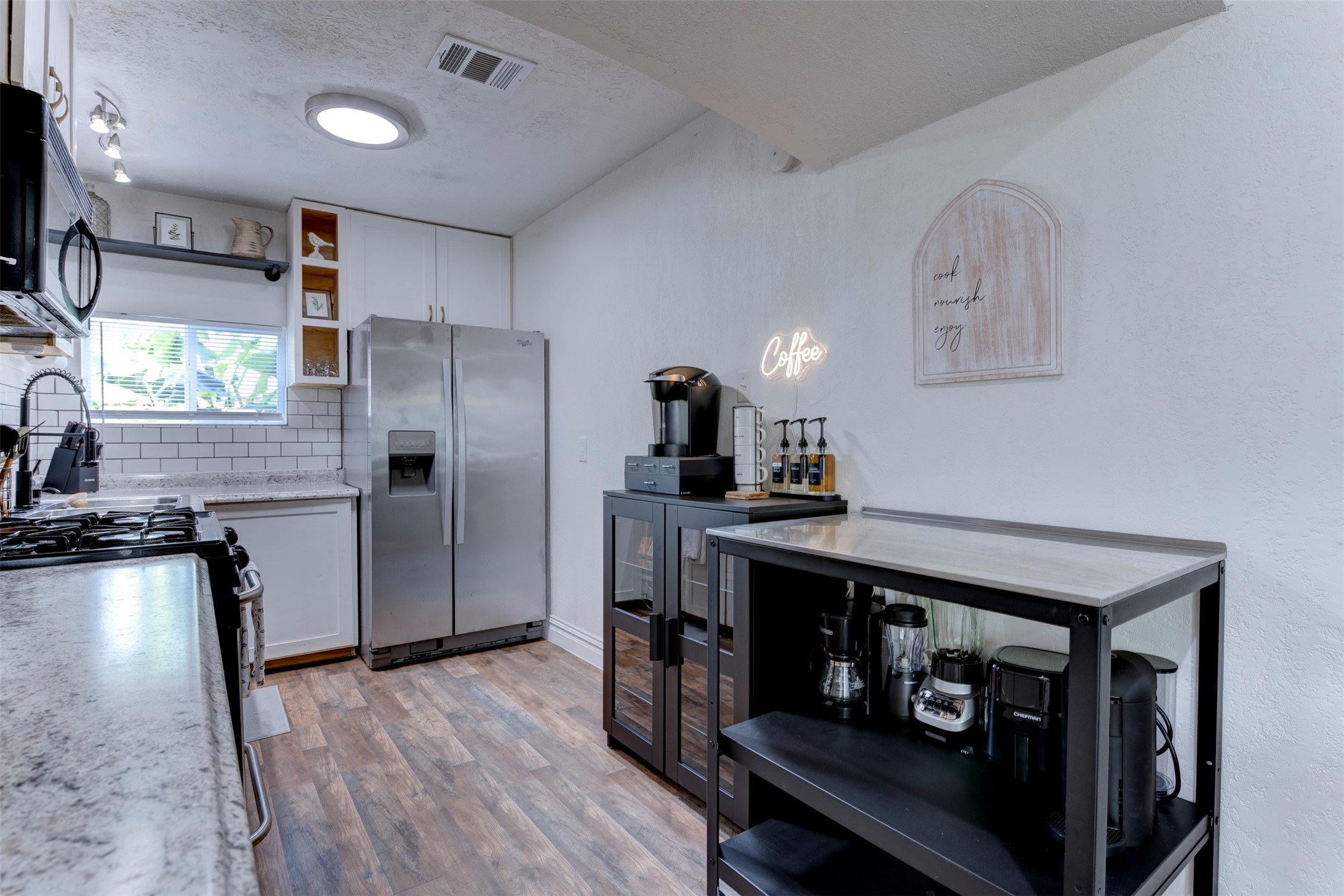 1121 Panama Street Houston, TX 77009 - Photo 14 of 35 Kitchen wide view with GE gas range, granite countertops, Whirlpool stainless side-by-side refrigerator with ice and water dispenser, white subway tile backsplash, white shaker upper cabinetry, open pine cubbies, matte black pull-down faucet, track lighting, flush mount ceiling light, and dedicated black metal coffee and appliance station with Keurig brewer and syrup dispensers.