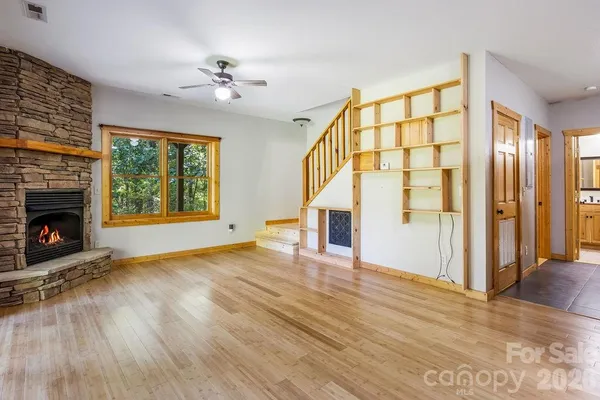 a view of an empty room with wooden floor fireplace and a window
