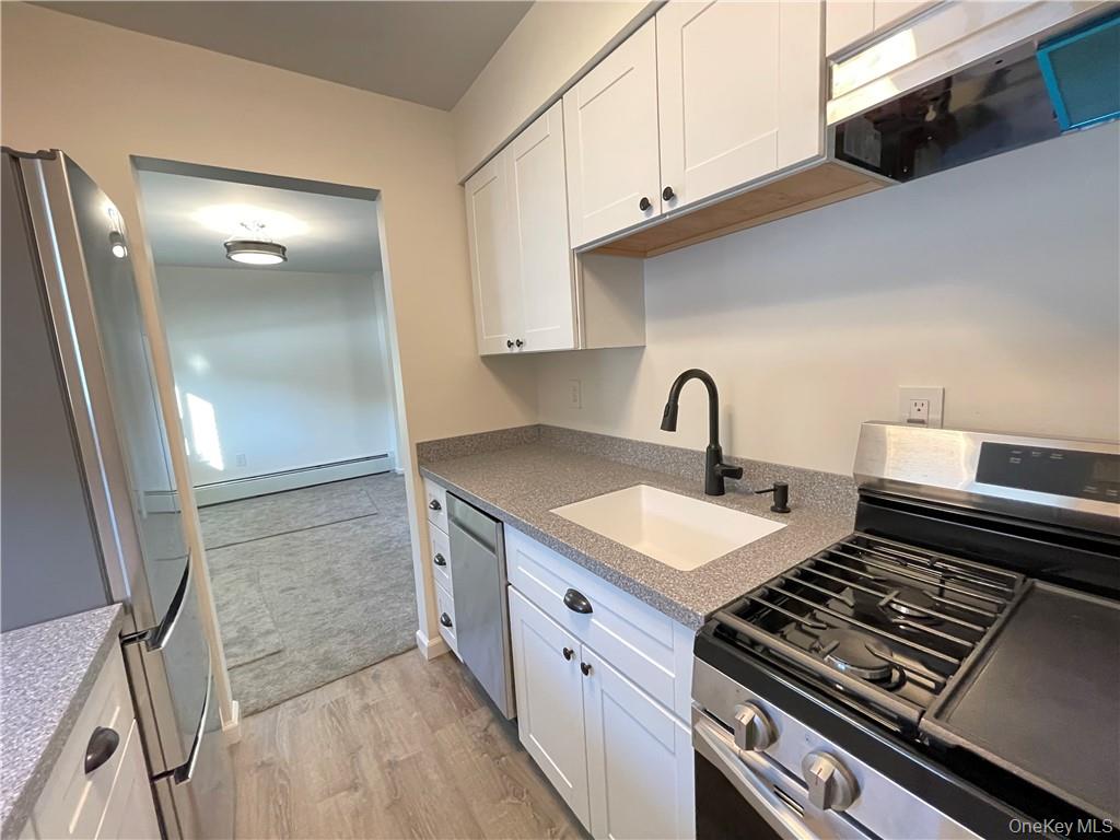 27 Tanager Road, Unit 2702 Monroe, NY 10950 - Photo 3 of 17 Kitchen featuring light wood-finish flooring, white cabinetry with dark hardware, speckled countertops, a matte black gooseneck faucet, and stainless steel appliances including a refrigerator, dishwasher, and gas range