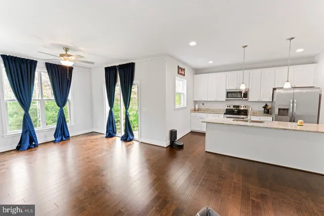 a kitchen with stainless steel appliances granite countertop a refrigerator a sink dishwasher a stove and a dining table with wooden floor