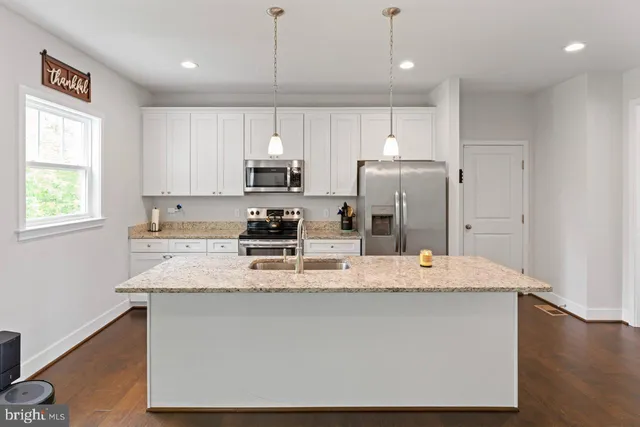 a kitchen with kitchen island granite countertop a stove a sink a refrigerator and white cabinets with wooden floor next to windows