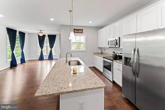 a kitchen with stainless steel appliances granite countertop a refrigerator a sink a stove and a wooden floors