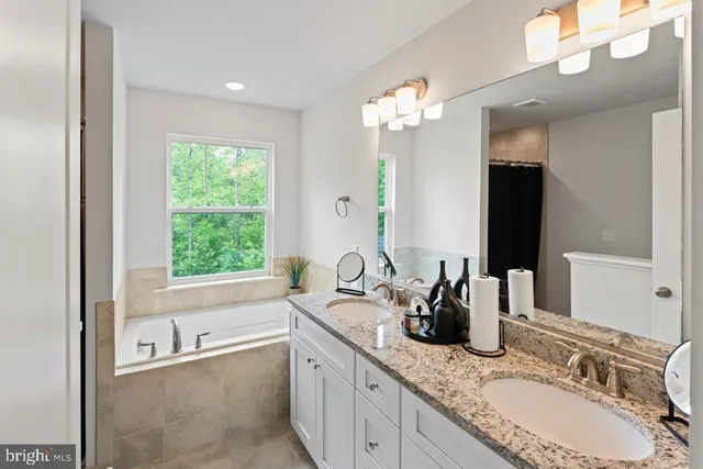 a bathroom with a granite countertop sink a large mirror and a bathtub next to a window