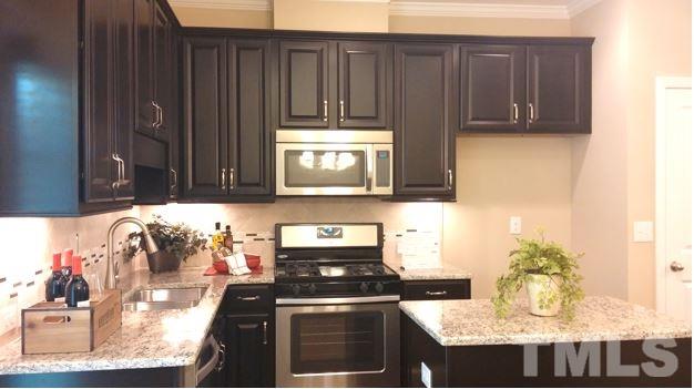 682 Wickham Ridge Road, Unit 145 Apex, NC 27539 - Photo 4 of 25 a kitchen with granite countertop wooden cabinets and a stove top oven