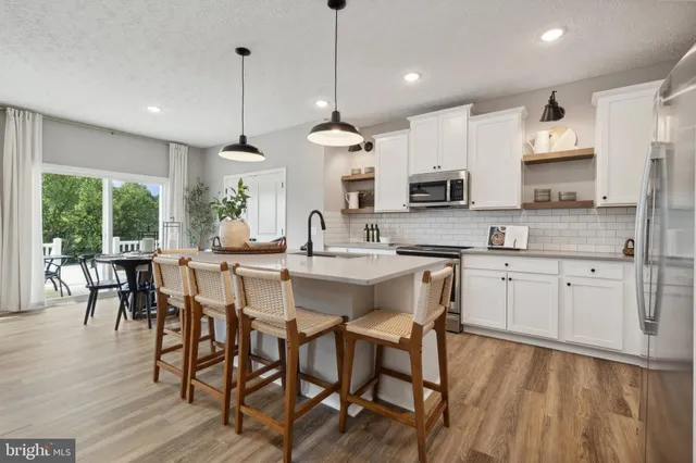 a kitchen with stainless steel appliances granite countertop a stove a sink a microwave a refrigerator a dining table and chairs with wooden floor