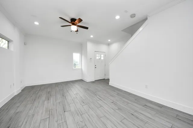 an empty room with wooden floor a ceiling fan and windows