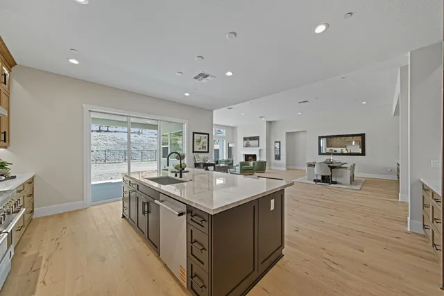 a large kitchen with stainless steel appliances a stove a sink dishwasher and a dining table with the view of living room