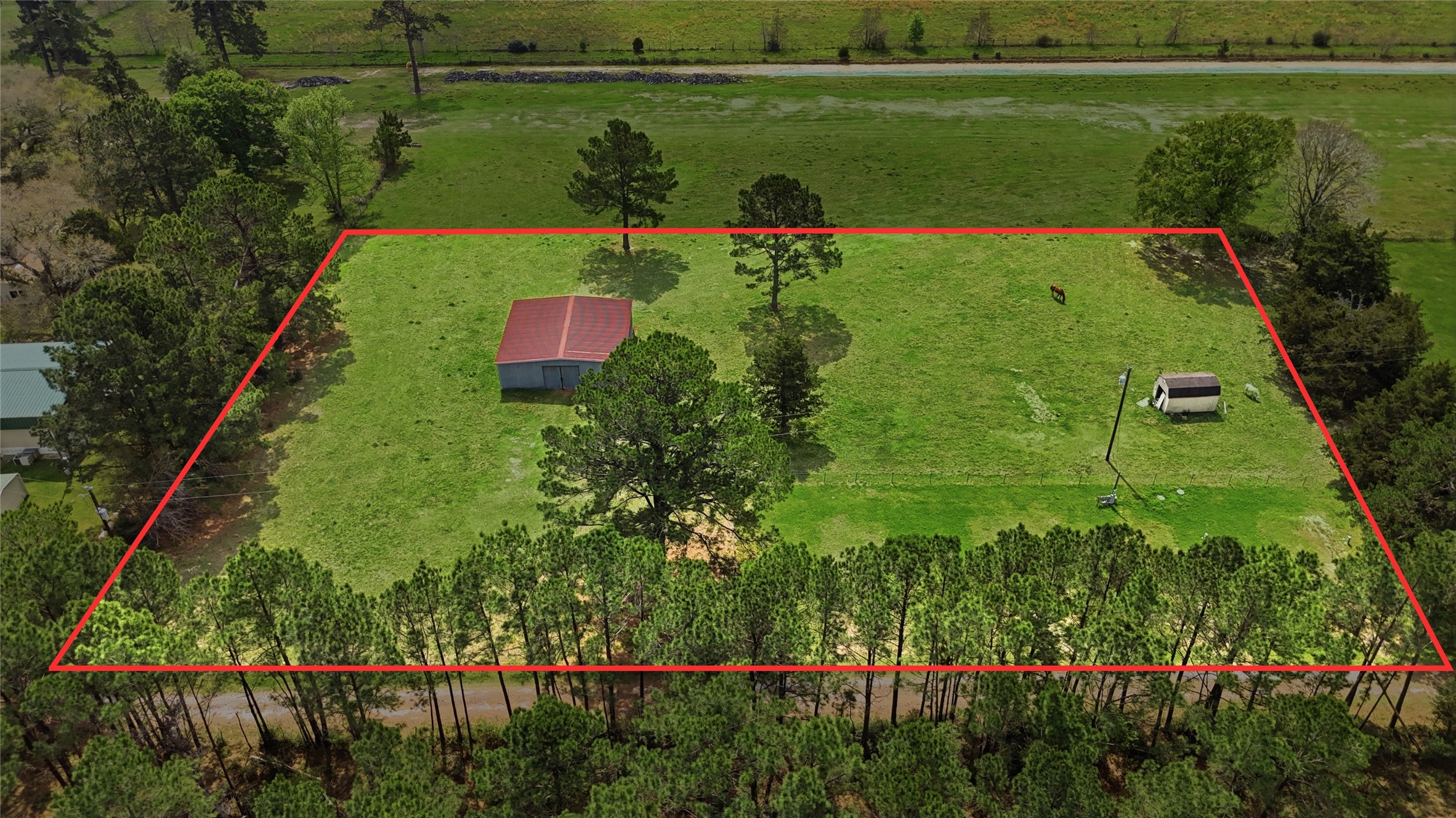 872 Four Notch Road Huntsville, TX 77340 - Photo 26 of 42 Expansive, tree-lined property featuring a spacious green lawn, a small outbuilding, and a charming red-roofed barn, offering ample space and privacy.