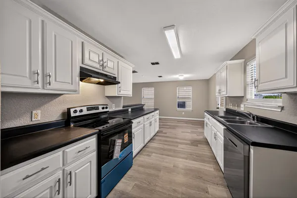 a large kitchen with stainless steel appliances granite countertop a stove a sink a refrigerator and white cabinets