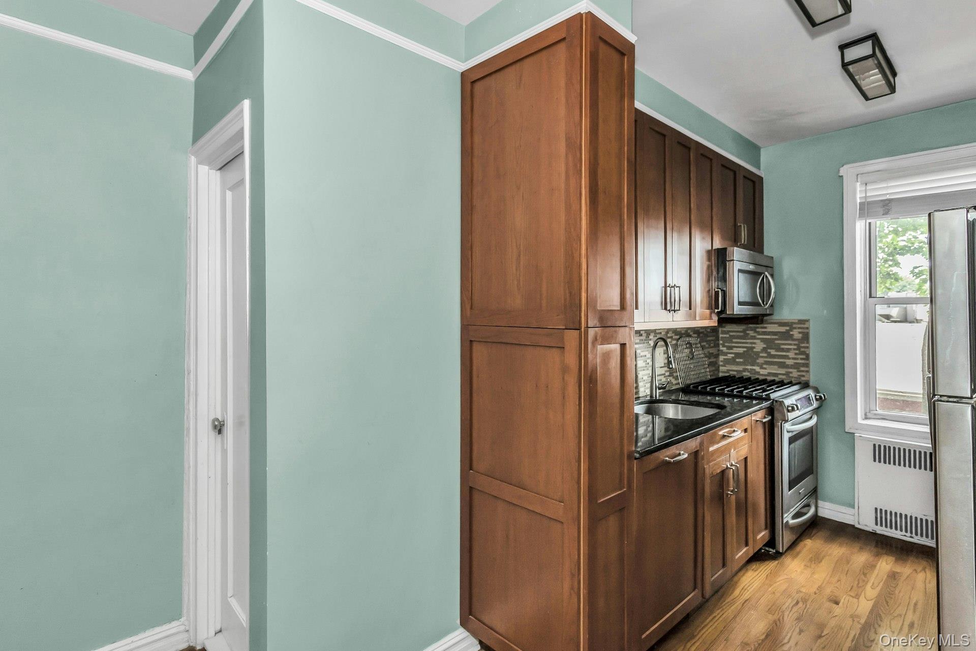 111-39 76th Road, Unit B7 Queens, NY 11375 - Photo 9 of 16 Kitchen with stainless steel appliances, radiator, backsplash, and light wood finished floors