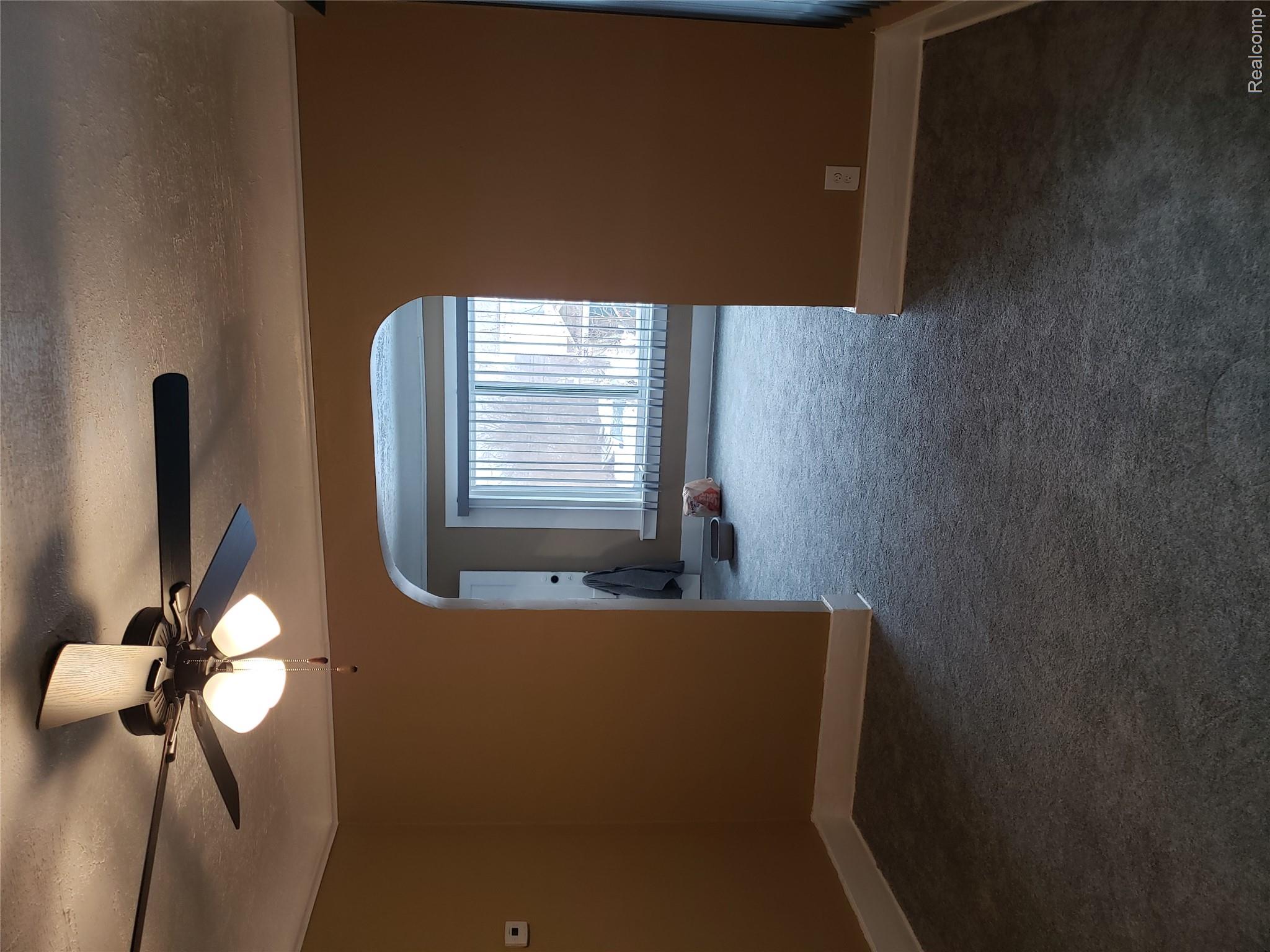 15381 Prairie Street Detroit, MI 48238 - Photo 12 of 22 Arched doorway leading to a room with multiple windows, featuring light filtering blinds, ceiling fan with integrated lighting, and neutral tone carpeting