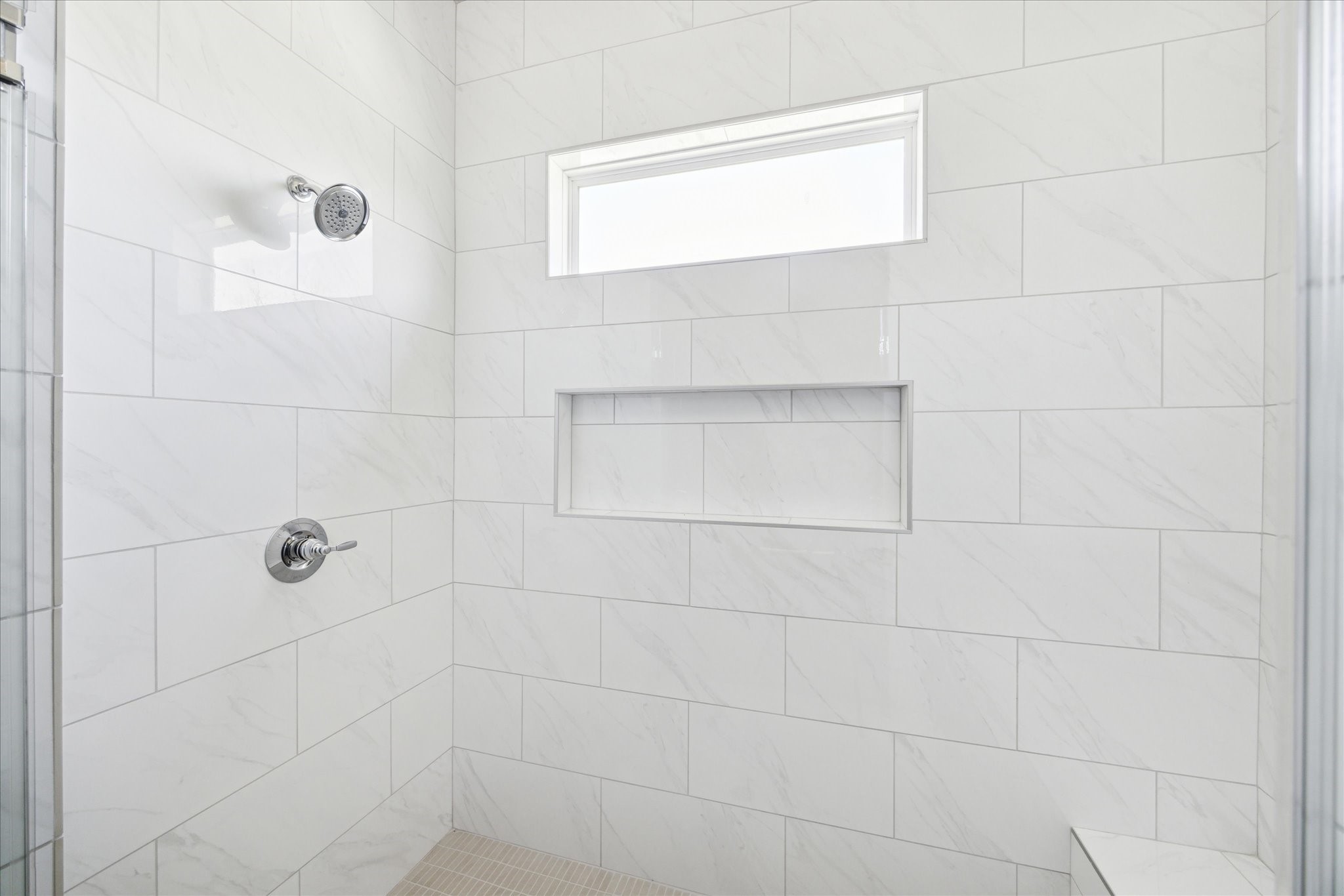 5309 Lambeth Riverside Drive Houston, TX 77091 - Photo 18 of 31 Thoughtfully Designed – This expansive primary shower, a comfortable seating bench, anchored by a mosaic floor, floor to ceiling tiled surround, storage niche, all elegantly enclosed in frameless glass.