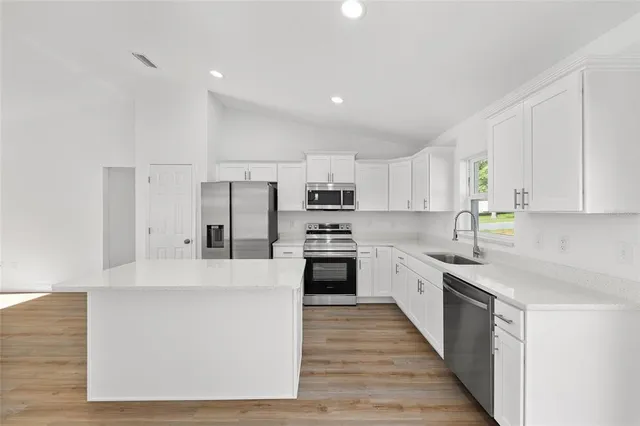 a large kitchen with stainless steel appliances granite countertop a stove top oven a sink and white cabinets