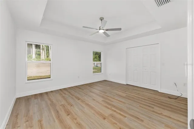 an empty room with wooden floor ceiling fan and windows