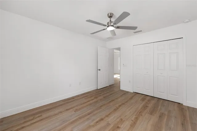 an empty room with wooden floor fan and windows