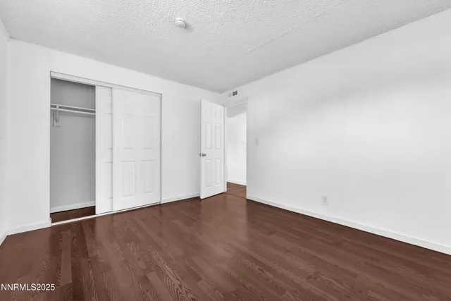 a view of an empty room with wooden floor and closet
