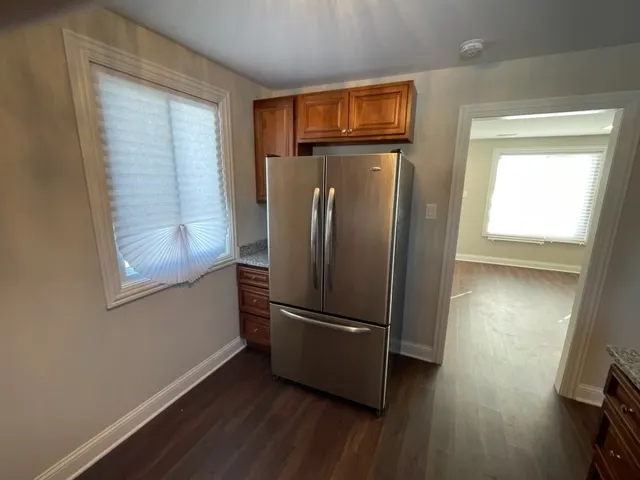 a view of a refrigerator in kitchen and an empty room with wooden floor