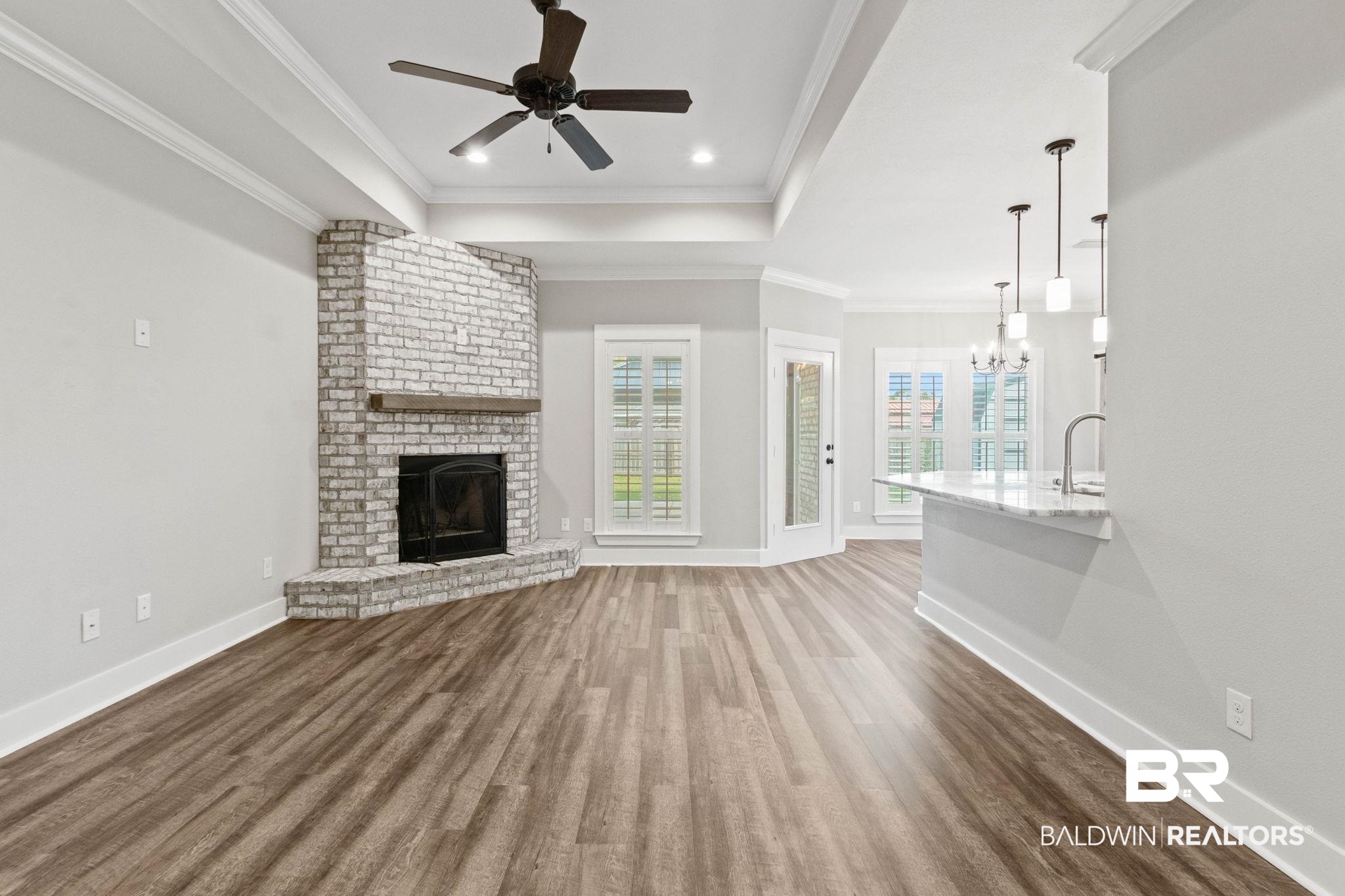 17376 Bankhead Boulevard Fairhope, AL 36532 - Photo 12 of 73 Unfurnished living room with a tray ceiling, a brick fireplace, dark wood-type flooring, crown molding, and ceiling fan