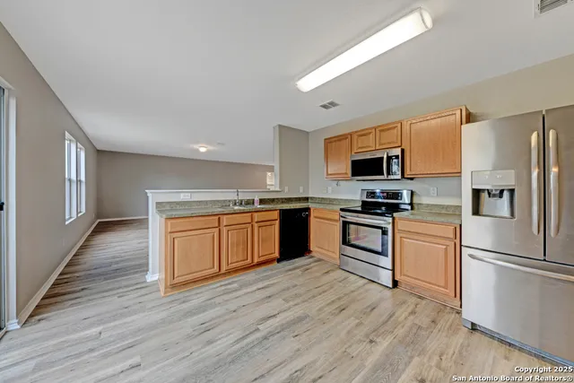 a kitchen with granite countertop a refrigerator oven a sink dishwasher a stove and white cabinets with wooden floor