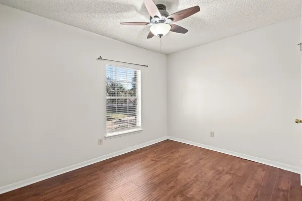 an empty room with wooden floor ceiling fan and window