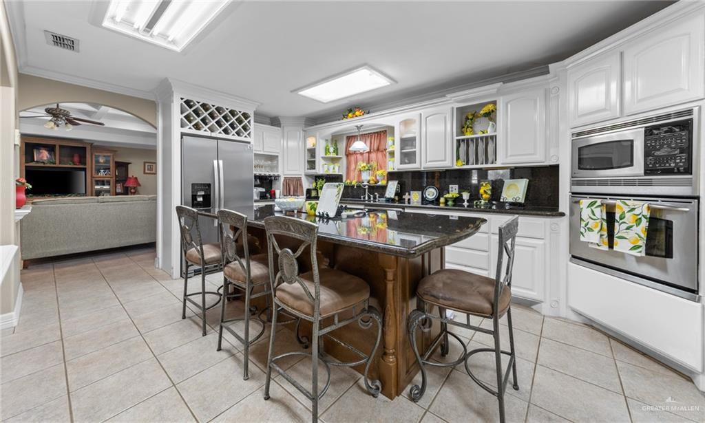 1514 Walnut Court Harlingen, TX 78550 - Photo 11 of 24 Dual tone kitchen with dark stone counters, light tile patterned floors, ornamental molding, stainless steel appliances, and a kitchen island