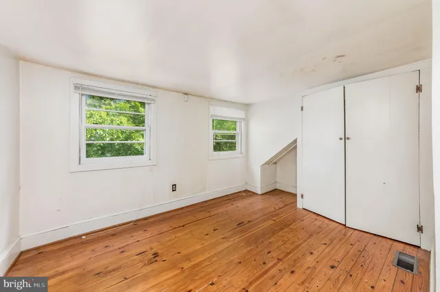 an empty room with wooden floor staircase and windows