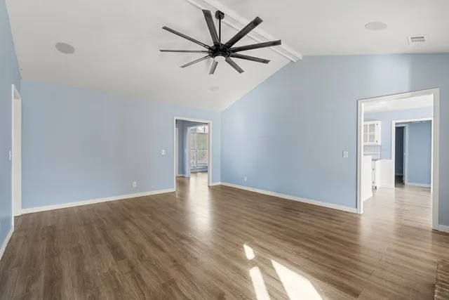a view of an empty room with wooden floor and a ceiling fan