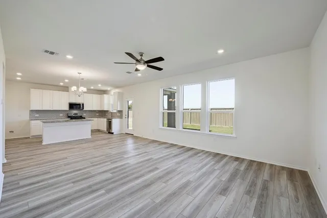 a view of an empty room with wooden floor and a kitchen