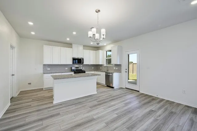 a view of a kitchen with granite countertop wooden floor stainless steel appliances and white cabinets