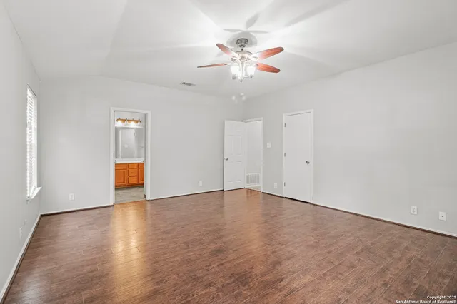an empty room with wooden floor fan and windows