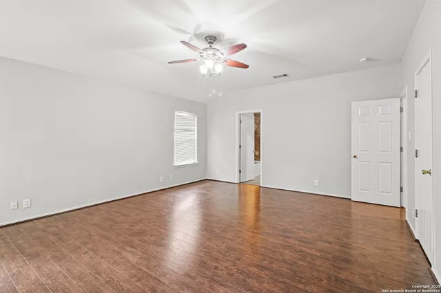 an empty room with wooden floor fan and windows