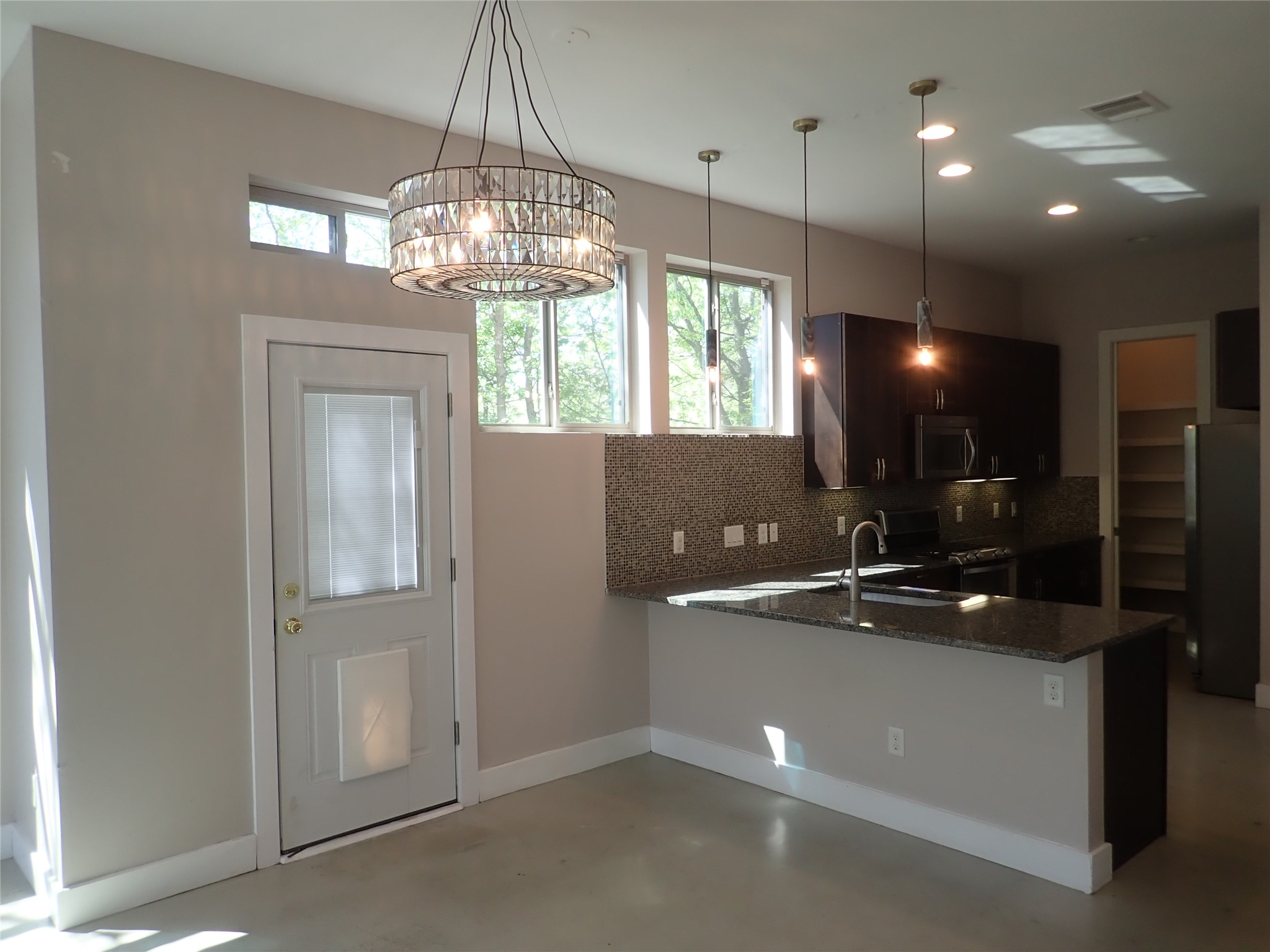 2912 East 14th Street, Unit A Austin, TX 78702 - Photo 8 of 27 Kitchen featuring dark stone counters, a peninsula, stainless steel appliances, decorative backsplash, and finished concrete floors