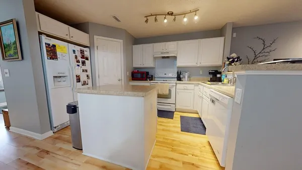 a kitchen with stainless steel appliances granite countertop a refrigerator a stove a sink dishwasher and white cabinets with wooden floor