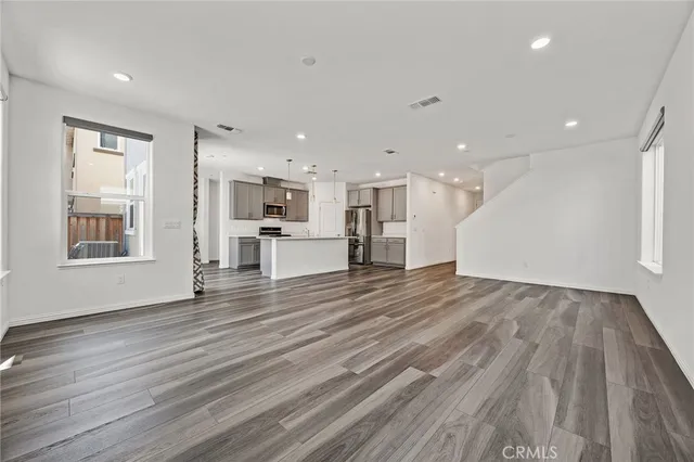 a view of an empty room with wooden floor and a kitchen