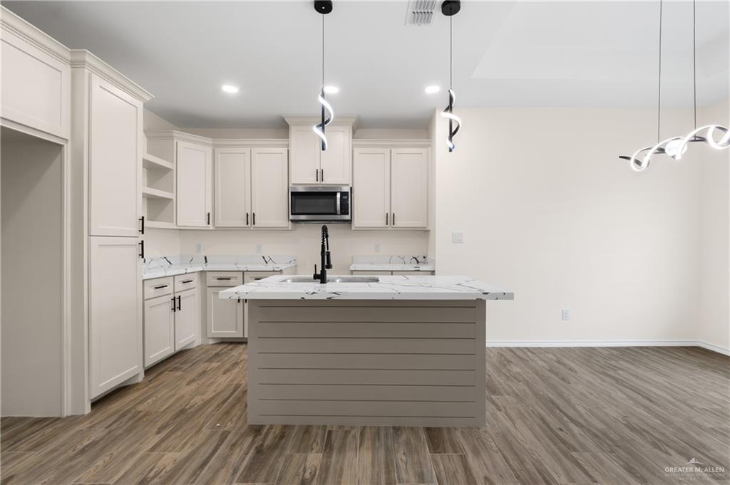 18054 Spruce Street Combes, TX 78552 - Photo 5 of 25 Spacious kitchen featuring an island with a stone-finish countertop, white cabinetry with black hardware, a built-in microwave, and wood-finish flooring