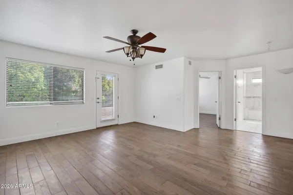a view of an empty room with wooden floor and a ceiling fan