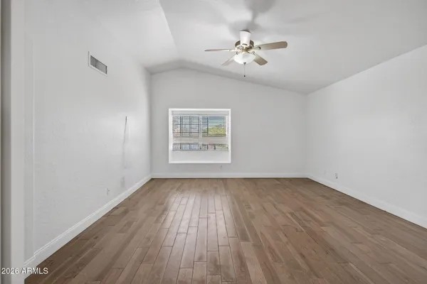 an empty room with wooden floor ceiling fan and windows