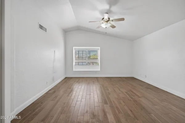 an empty room with wooden floor ceiling fan and windows