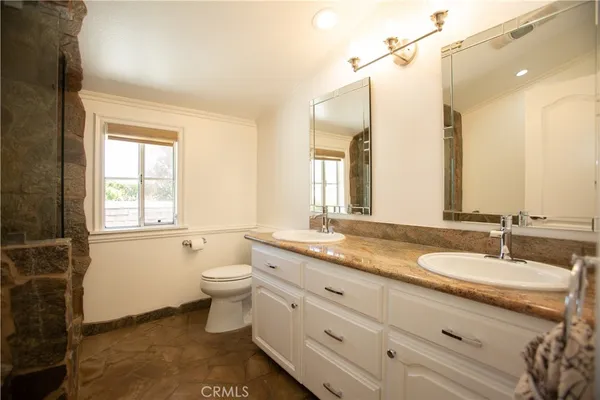 a bathroom with a granite countertop double vanity sink a mirror and a toilet
