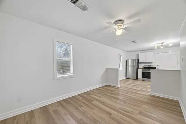 an empty room with wooden floor fan and windows