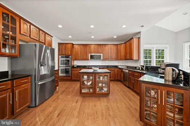 a kitchen with stainless steel appliances granite countertop a refrigerator a stove top oven a sink dishwasher and wooden cabinets with wooden floor