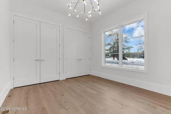an empty room with wooden floor and way to kitchen