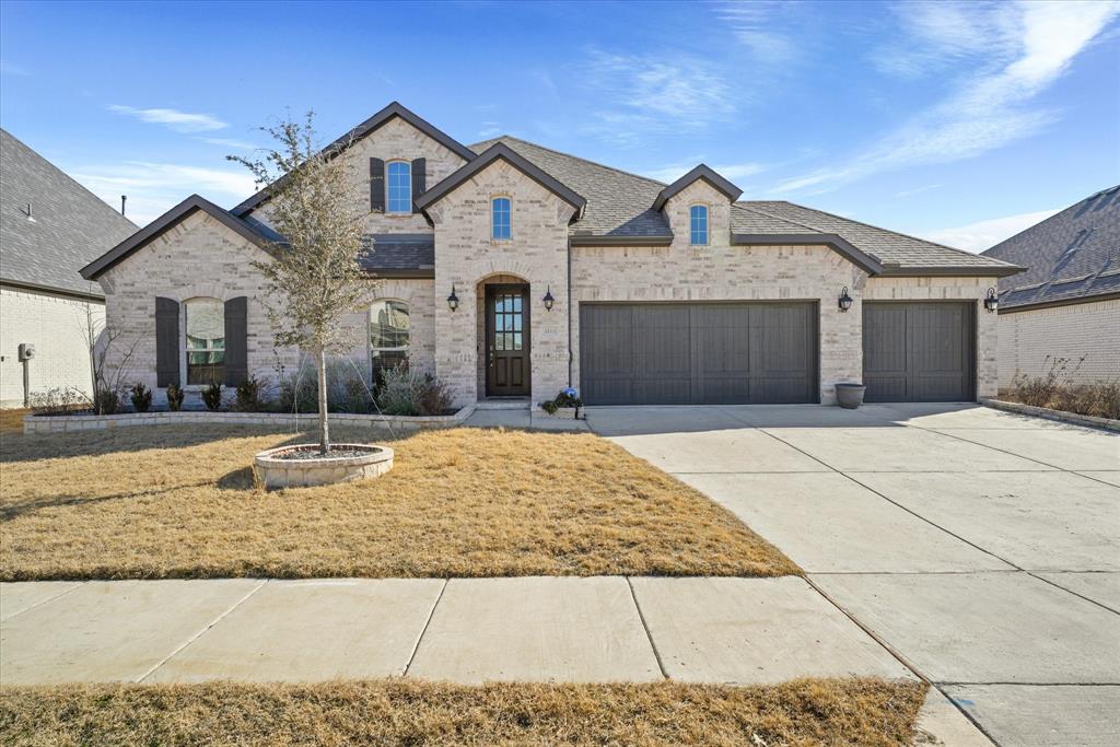French country home featuring driveway, a shingled roof, an attached garage, and brick siding