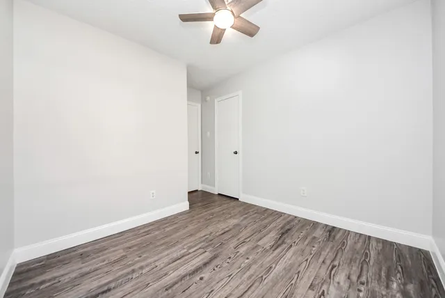 an empty room with wooden floor fan and windows